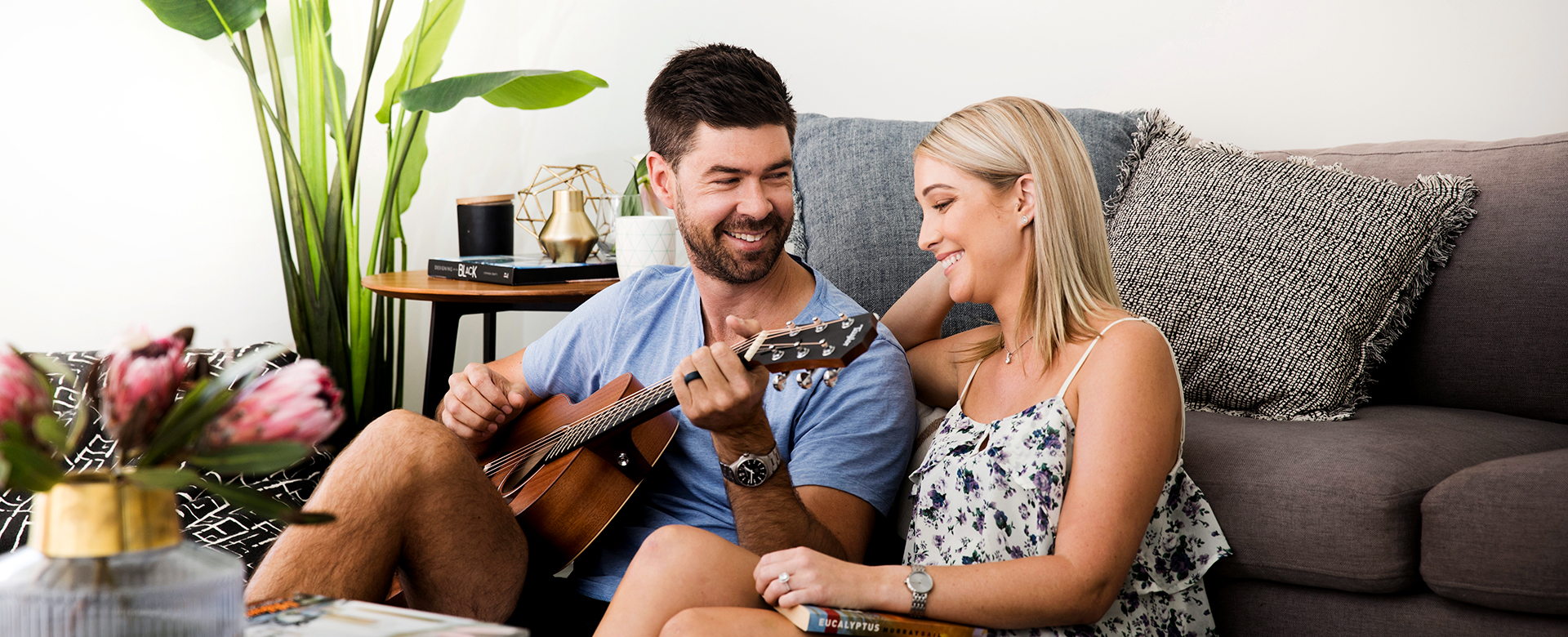 Couple playing guitar sitting in living room of their Evergreen home by AVJennings Family sitting on couch in their Evergreen home by AVJennings,  located in Spring Farm, NSW 2570. Houses for sale spring farm, house and land packages Spring Farm.